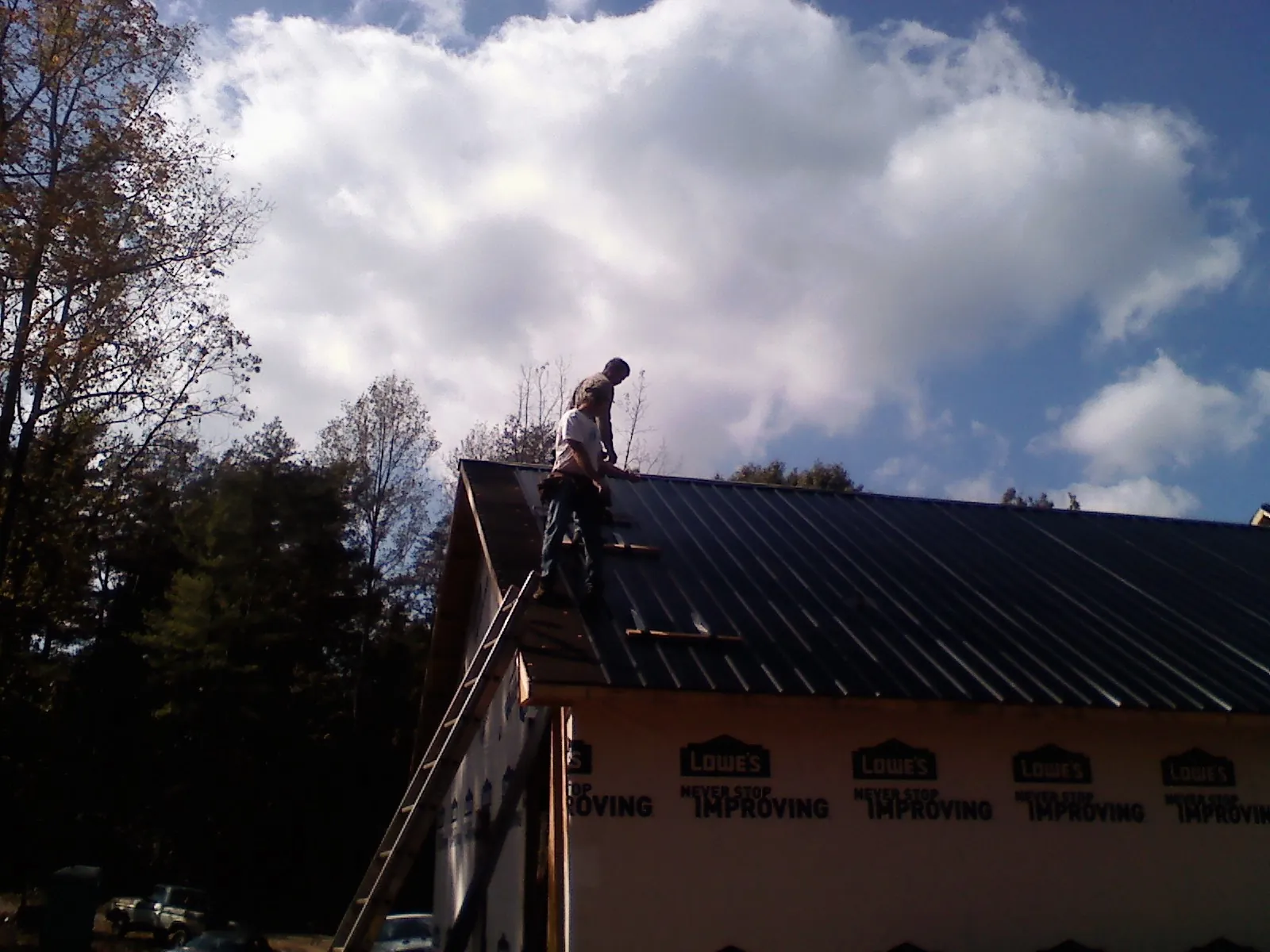 Roofer fastening dark metal panels high against a cloudy sky, from a Roof Inspection job in Alton