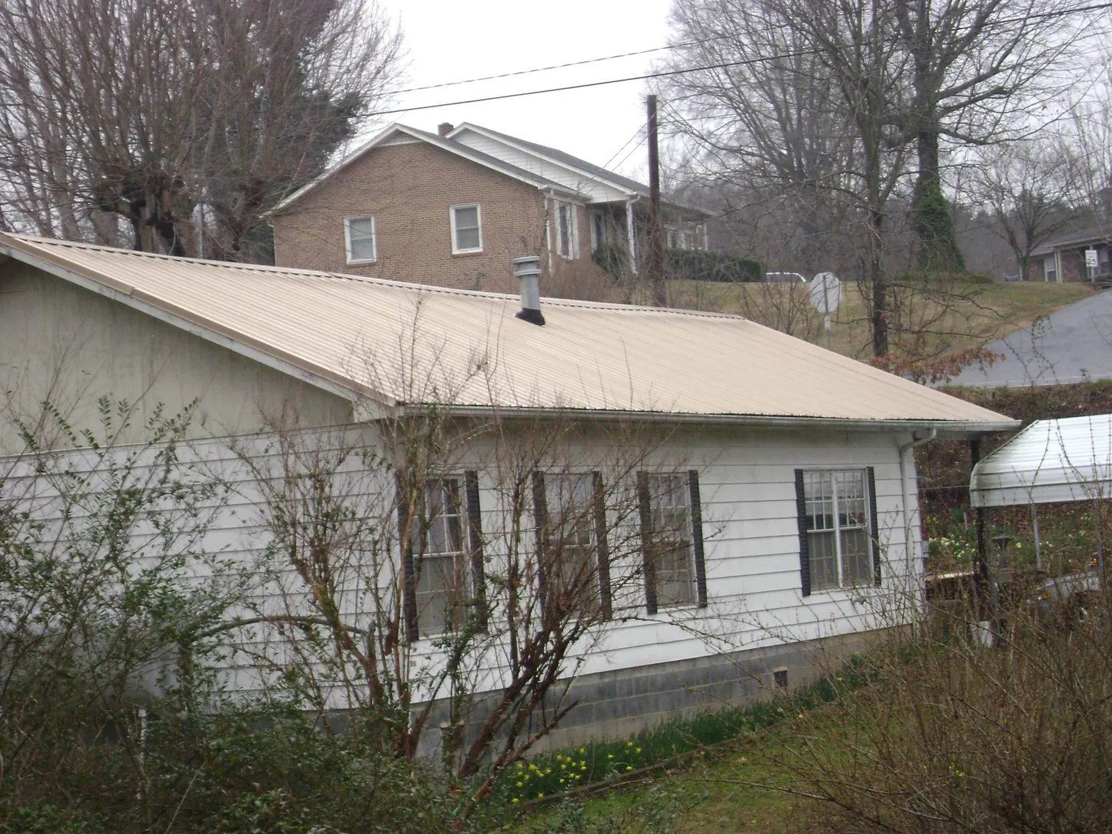 Tan metal roof on a white sided house set into a hillside — Commercial Roofing by Roofing Brothers in Alton